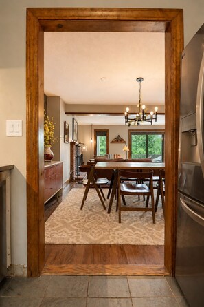 A dining area with a wooden table and chairs, a chandelier, and a view of the outdoors.