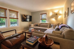 Ein Wohnzimmer mit einer Couch, einem Couchtisch mit Büchern, einer Holzkugel und einem an der Wand befestigten Fernseher.
