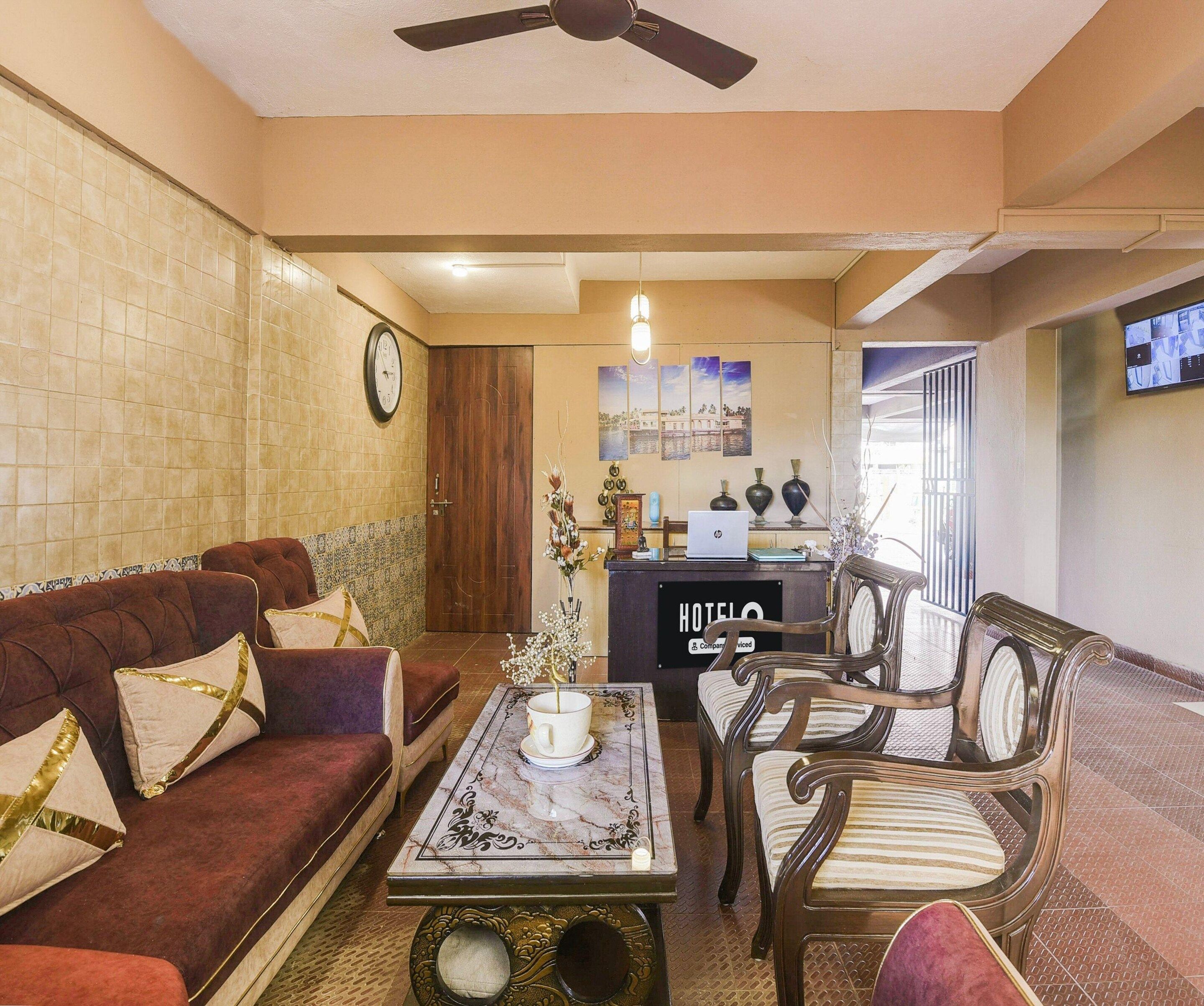 A hotel lobby with a sofa, chairs, a coffee table, a reception desk, a clock, and a ceiling fan.