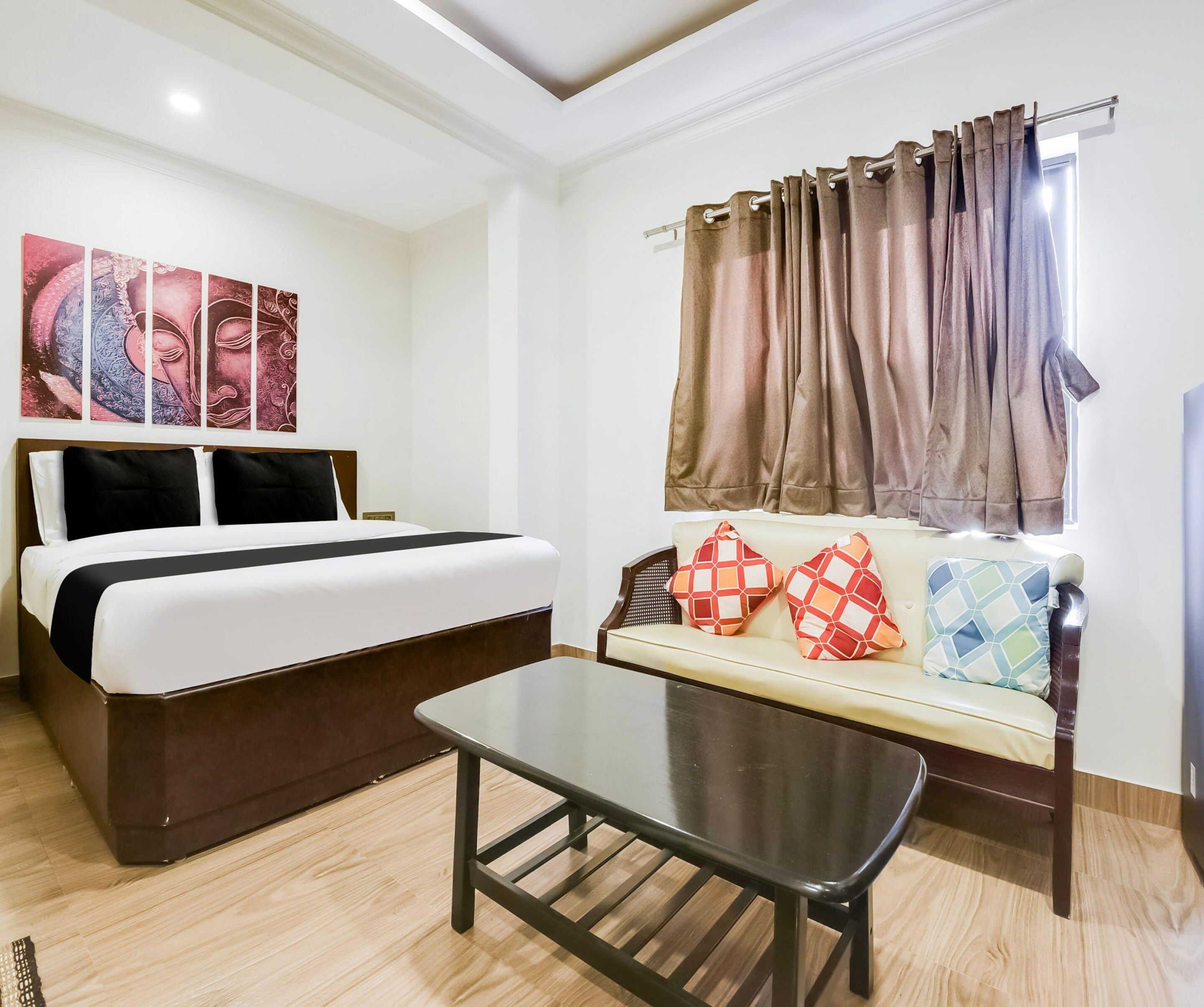 A hotel room with a bed, a sofa with patterned cushions, a coffee table, and a window with curtains.