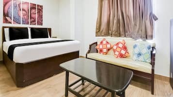 A hotel room with a bed, a sofa with patterned cushions, a coffee table, and a window with curtains.
