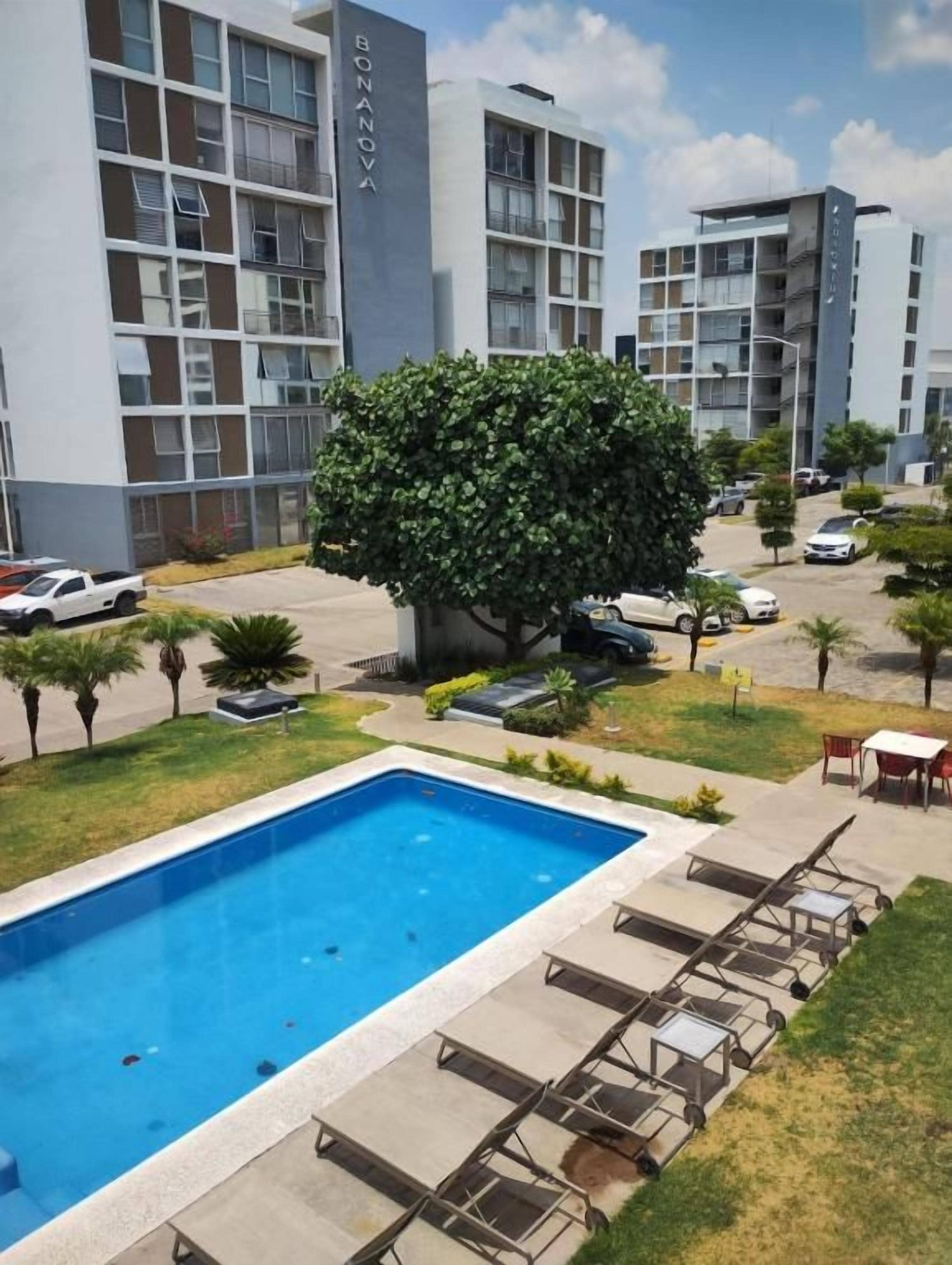 Un hotel moderno con piscina, sillas de descanso y un jardín bien cuidado.