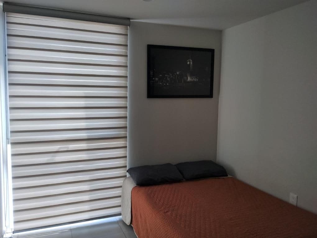 A bedroom with a bed, a window with blinds, and a framed picture on the wall.
