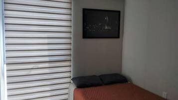 A bedroom with a bed, a window with blinds, and a framed picture on the wall.