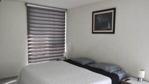Una camera da letto con un letto, un comodino, una lampada, un quadro appeso alla parete e una finestra con persiane.