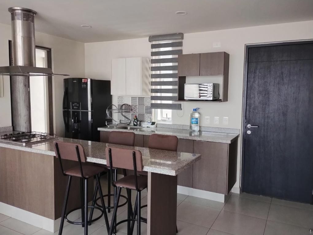 Una cocina moderna con una isla central, taburetes de bar, estufa integrada y microondas.