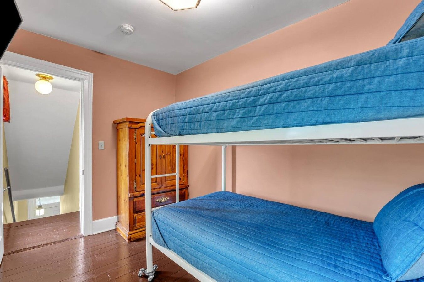 A bunk bed room with a wooden wardrobe and a door leading to another room.
