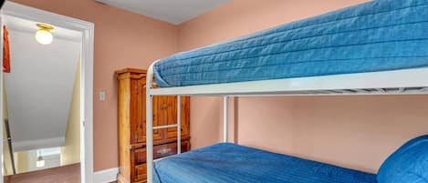 A bunk bed room with a wooden wardrobe and a door leading to another room.