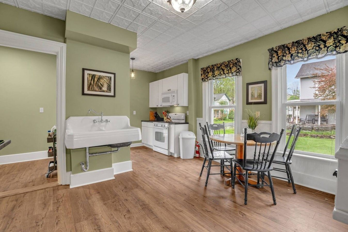A kitchen with a white sink, white cabinets, a dining table with chairs, and a view of the outside.