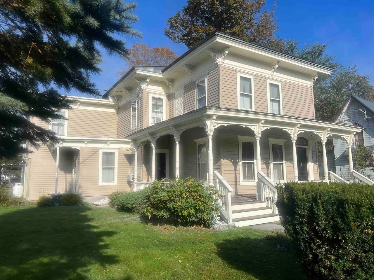A two-story house with a front porch, a small front yard, and a tree.