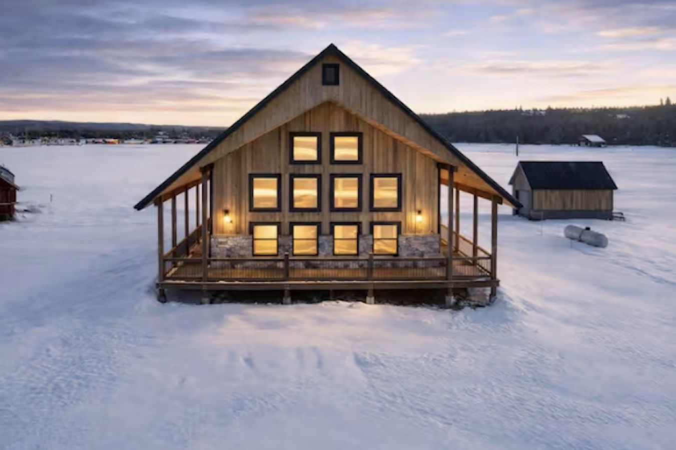 A wooden cabin with a porch and multiple windows, surrounded by snow.