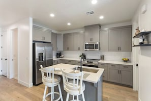 A modern kitchen with grey cabinets, stainless steel appliances, and a central island with bar stools. - Pool, PickleBall, xBox, Dog Friendly close to Zion National Park (Washington)