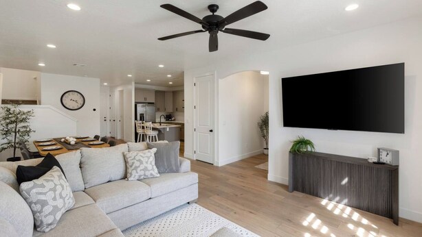 Ein modernes Wohnzimmer mit Deckenventilator, Flachbildfernseher und Essbereich mit einer Uhr.