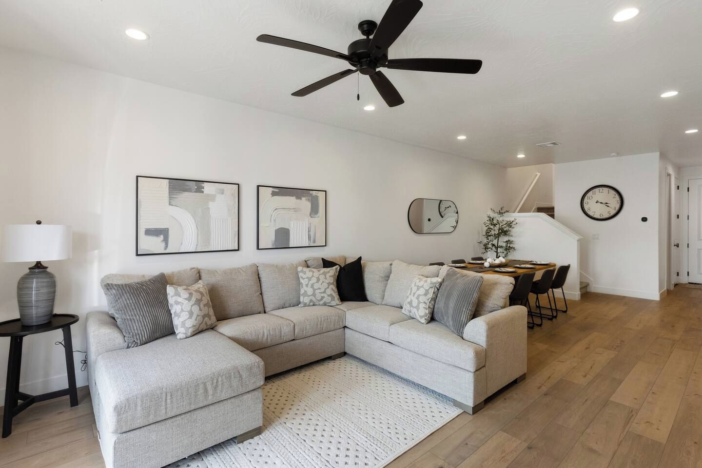 Una sala de estar con un sofá modular, un ventilador de techo y un comedor con mesa y sillas.