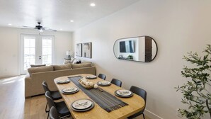 Ein Essbereich mit einem Holztisch, gedeckt für sechs Personen, einer Couch, einem Deckenventilator und einem großen Spiegel an der Wand.