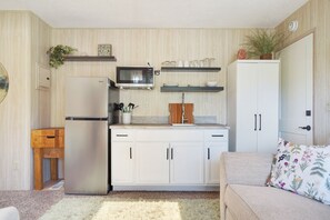 A compact kitchen with a refrigerator, microwave, and white cabinets.