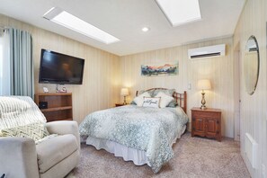A bedroom with a bed, a TV, a chair, a lamp, and a painting on the wall.