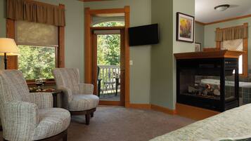A room with two upholstered chairs, a small table with a glass of wine, a fireplace, and a television mounted on the wall.