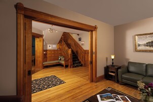 Un salón amplio con una escalera de madera, un sofá verde y una lámpara sobre una mesita auxiliar.