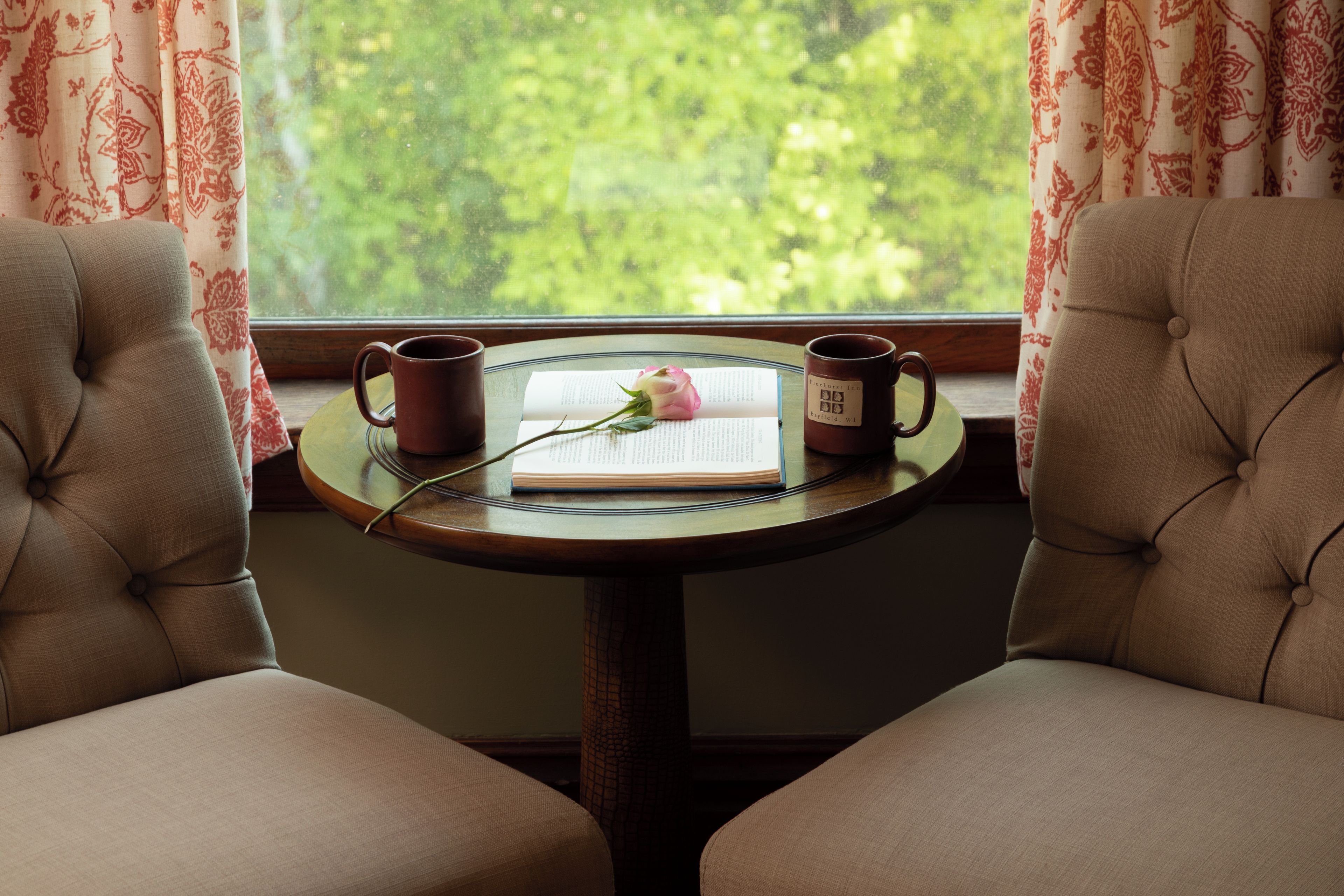 Een knus hoekje om te lezen, met twee comfortabele fauteuils, een klein rond tafeltje, een boek, een roos en twee mokken.