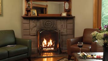 A cozy living room with a fireplace, leather sofas, and a table with a glass of wine and a fruit platter.
