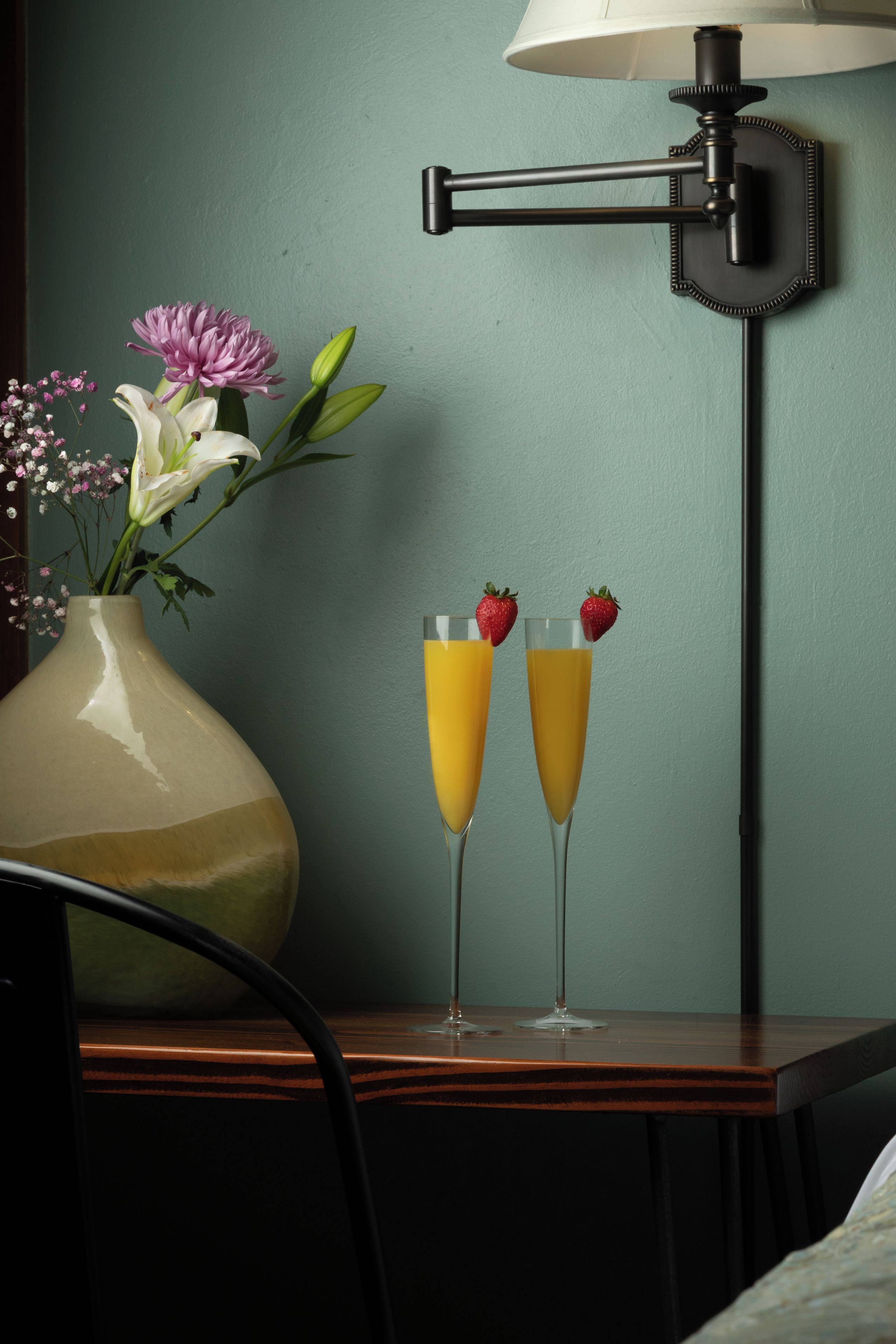 A table with a vase of flowers and two glasses of orange juice with strawberries on top.