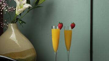 A table with a vase of flowers and two glasses of orange juice with strawberries on top.