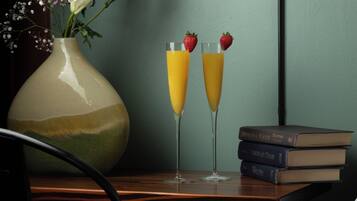 Deux verres de jus d’orange avec des fraises, posés sur une table, à côté d’un vase rempli de fleurs et d’une pile de livres.