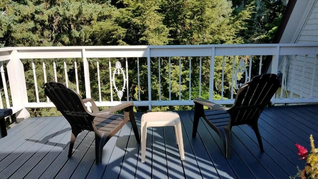 A wooden deck with two Adirondack chairs and a small stool, surrounded by a white railing.