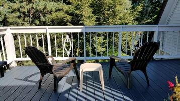 A wooden deck with two Adirondack chairs and a small stool, surrounded by a white railing.