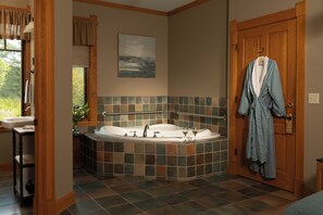 A bathroom with a bathtub, a sink, and a robe hanging on the door. - Pinehurst Inn - Luxury Bayfield Hotel (Bayfield)