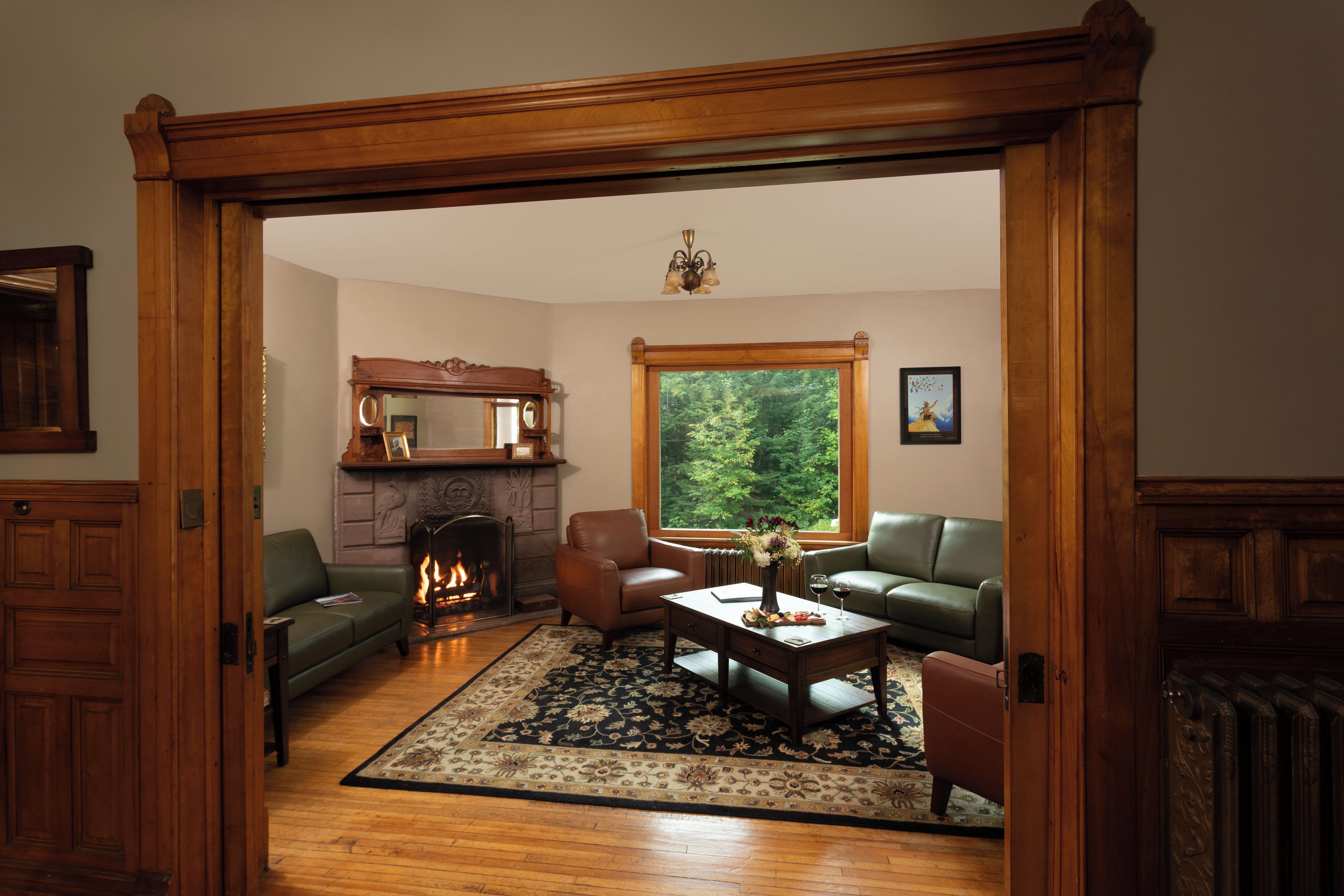A living room with a fireplace, leather sofas, a coffee table, and a large window with a forest view.