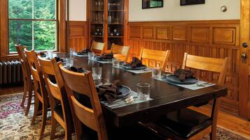 A dining room with a wooden table set for six, surrounded by chairs, with a chandelier above and a cabinet with glass doors to the side.