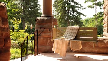 A bench with a knitted blanket and a book, set against a stone wall with a metal railing, surrounded by greenery.