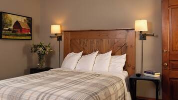 A neatly made bed with a plaid bedspread, flanked by two bedside tables with lamps, a vase of flowers, and a painting on the wall.