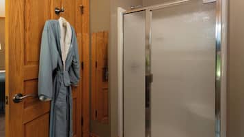 A bathroom with a wooden door, a glass shower enclosure, and a robe hanging on the door.