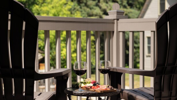 A wooden deck with two chairs and a small table with a glass of red wine and a plate of food. - Pinehurst Inn - Luxury Bayfield Hotel (Bayfield)