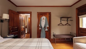 A bedroom with a bed, a bedside table, a lamp, a wardrobe, a hanging clothes rack, and a bench. - Pinehurst Inn - Luxury Bayfield Hotel (Bayfield)