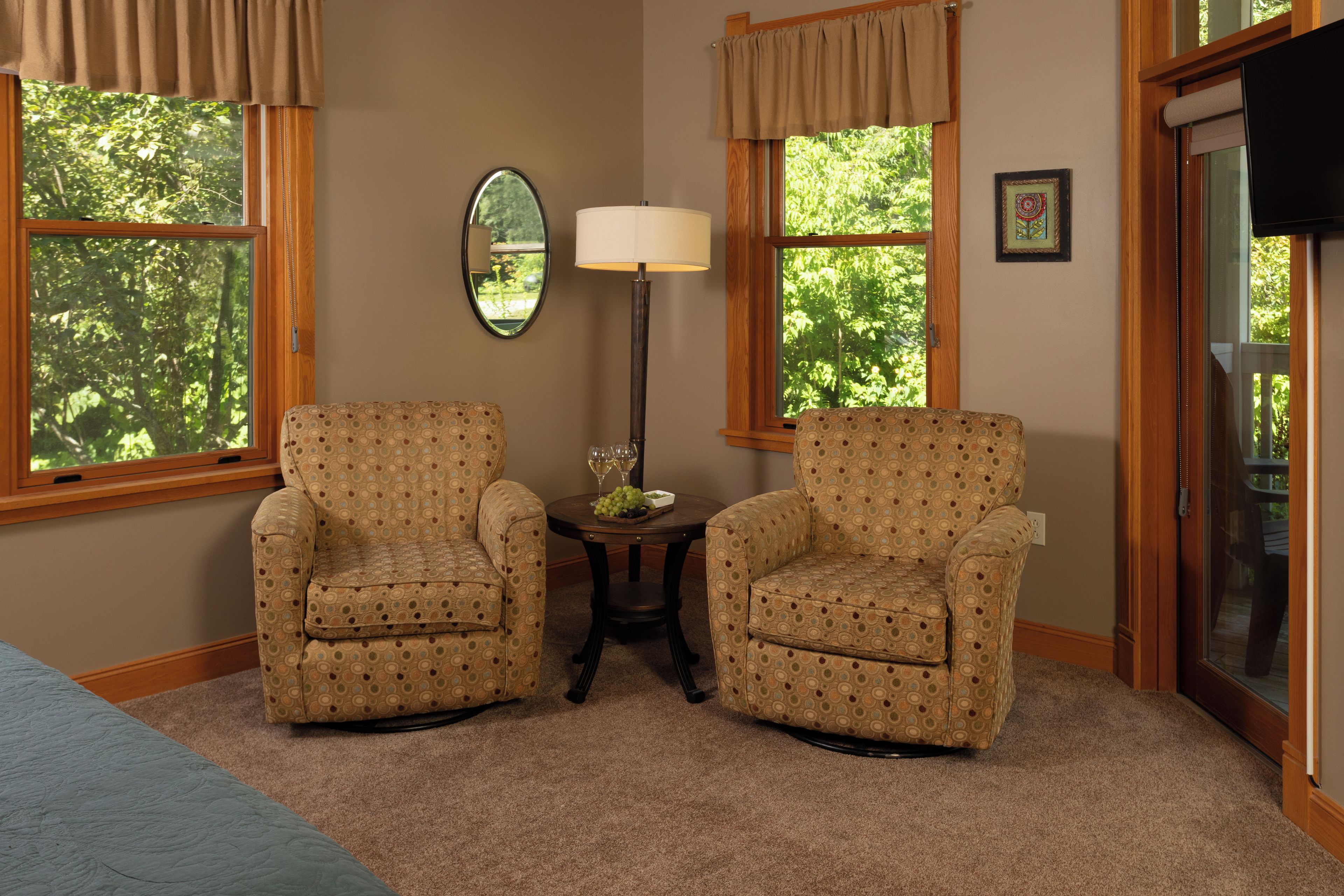 A room with two patterned armchairs, a small table with a lamp, and a mirror on the wall.