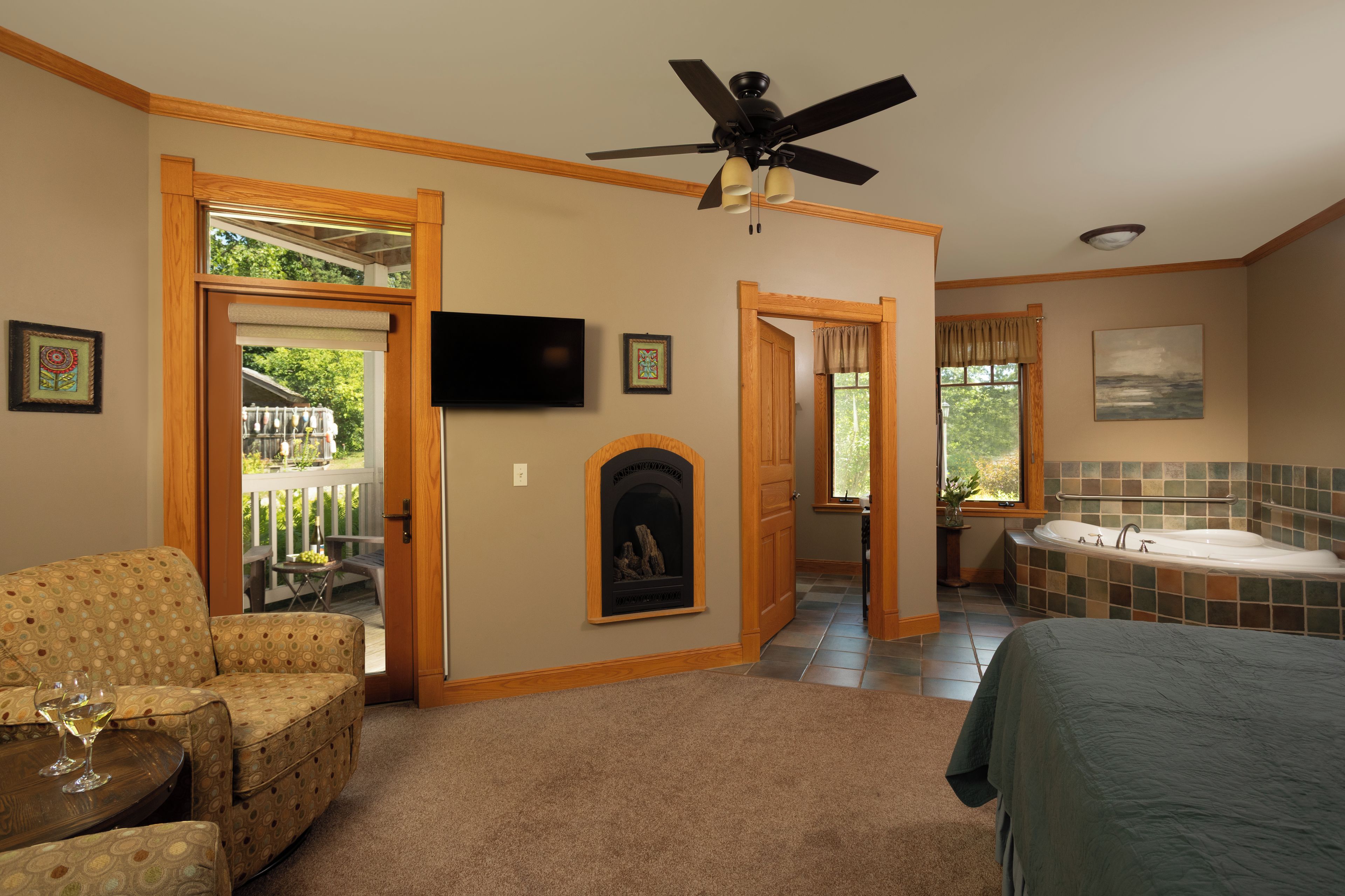 A bedroom with a bed, a ceiling fan, a fireplace, a TV, and a bathroom with a bathtub.