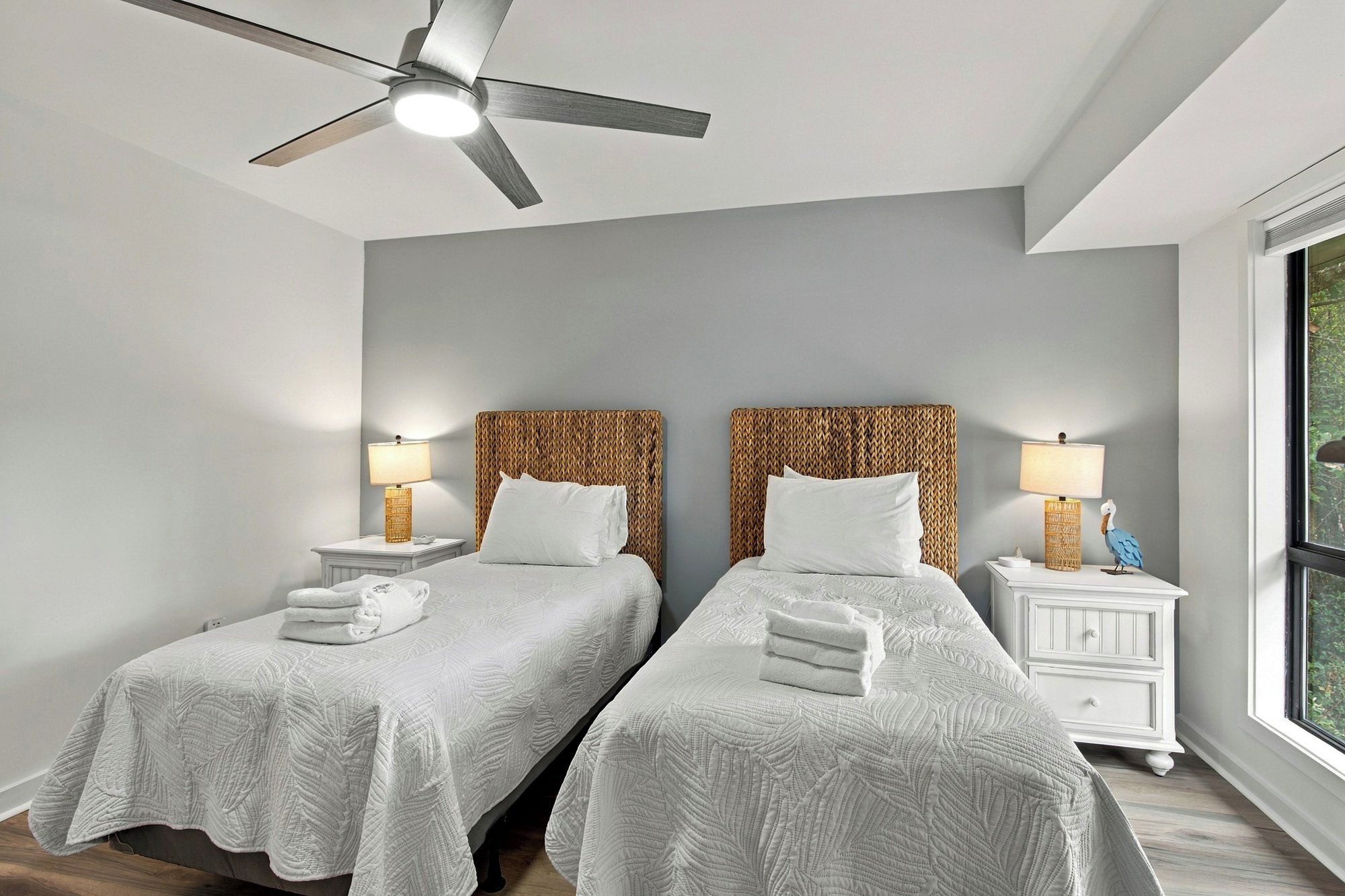 A hotel room with two beds, a ceiling fan, bedside lamps, and a window with a view.