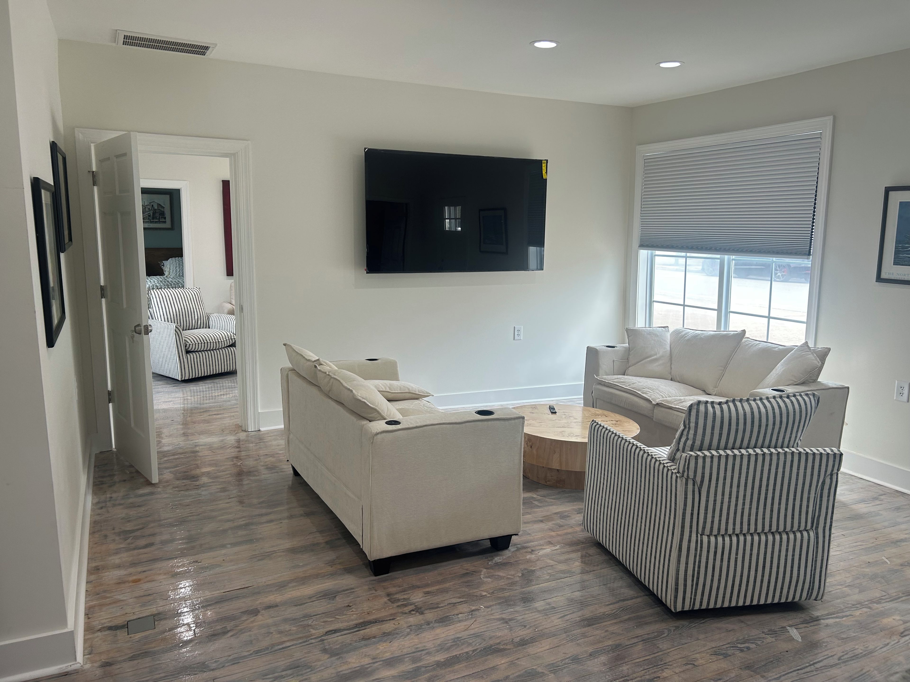 A modern living room with a flat-screen TV mounted on the wall, a sofa, a striped armchair, and a coffee table.