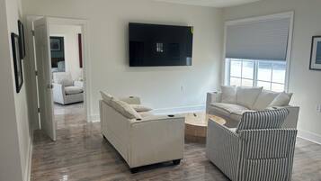 A modern living room with a flat-screen TV mounted on the wall, a sofa, a striped armchair, and a coffee table.