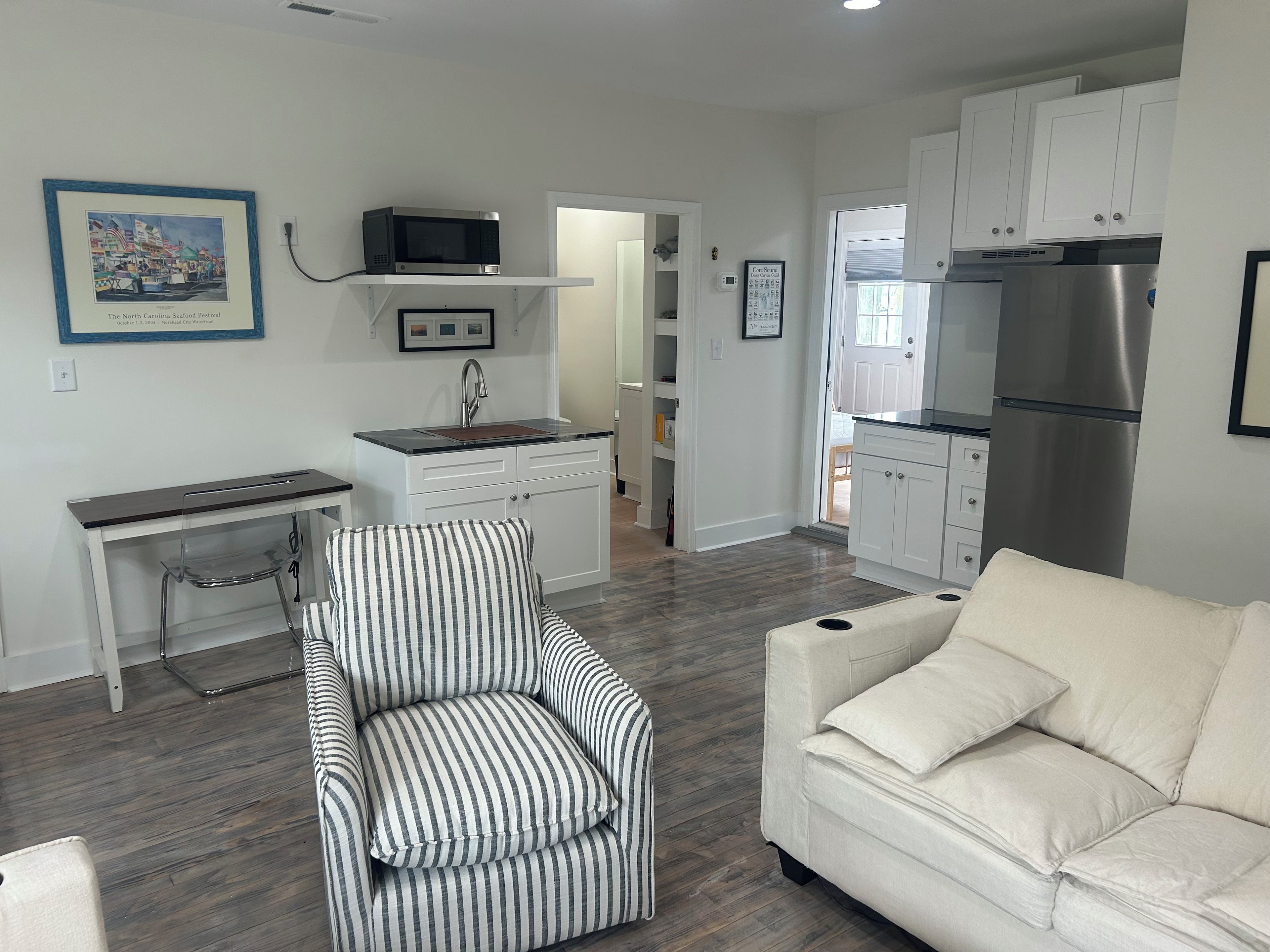 A compact living space with a kitchenette, a striped armchair, a white sofa, and a framed picture on the wall.