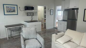 A compact living space with a kitchenette, a striped armchair, a white sofa, and a framed picture on the wall.