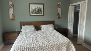 A bedroom with a large bed, two nightstands, a wooden headboard, a framed picture on the wall, and a door leading to another room. - Waterfront luxury with boat dock accessibility (Morehead City)