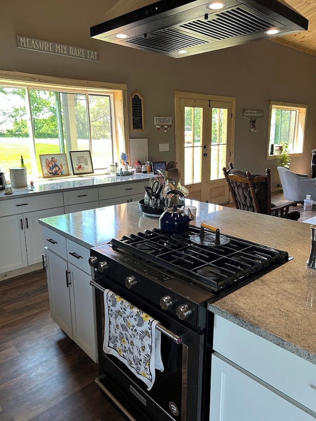 Una cocina con una isla central, estufa y comedor con una silla.