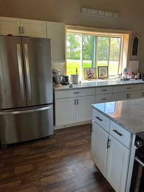 A kitchen with white cabinets, a stainless steel refrigerator, and a window with a view of greenery.