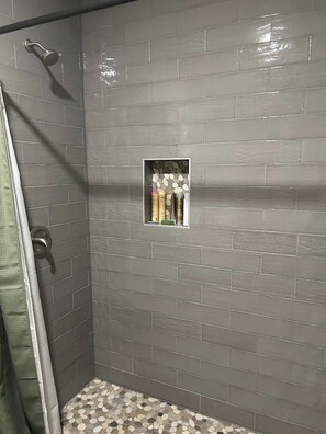 Eine Dusche mit Glastür, eine kleine Ablage mit Toilettenartikeln und ein Boden mit Kieselmuster.