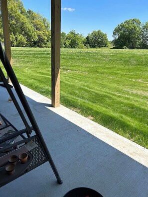A patio area with a concrete floor, a metal table with a metal chair, and a view of a well-maintained lawn.